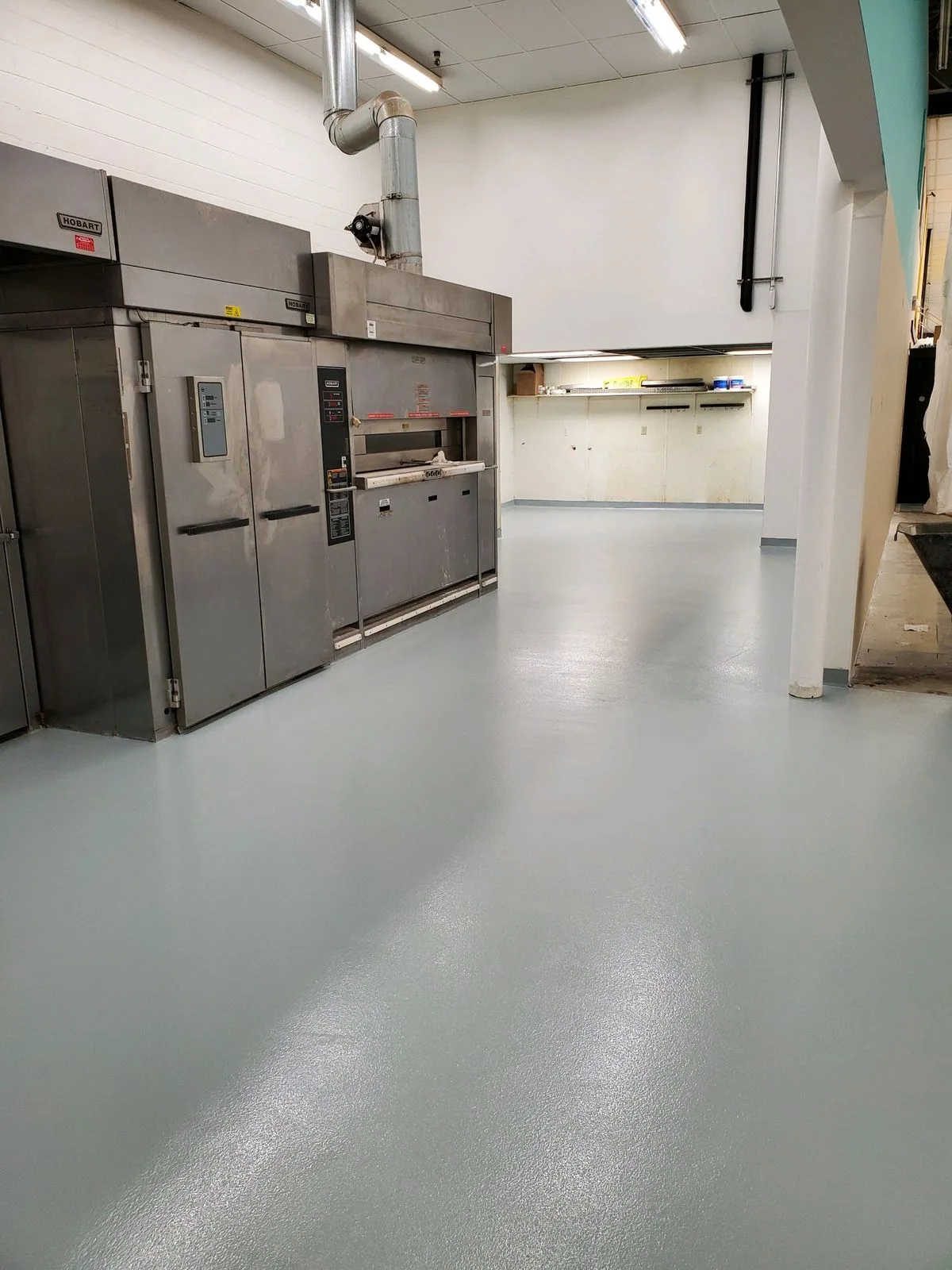 Boulangerie industrielle avec plans de travail en bois sur structure inox, gaufres empilées sur étagères et laminoir, sol béton gris