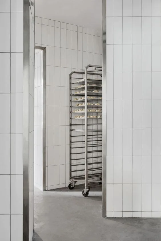 Boulangerie artisanale avec chariots inox contre mur carrelé blanc, joints visibles au sol