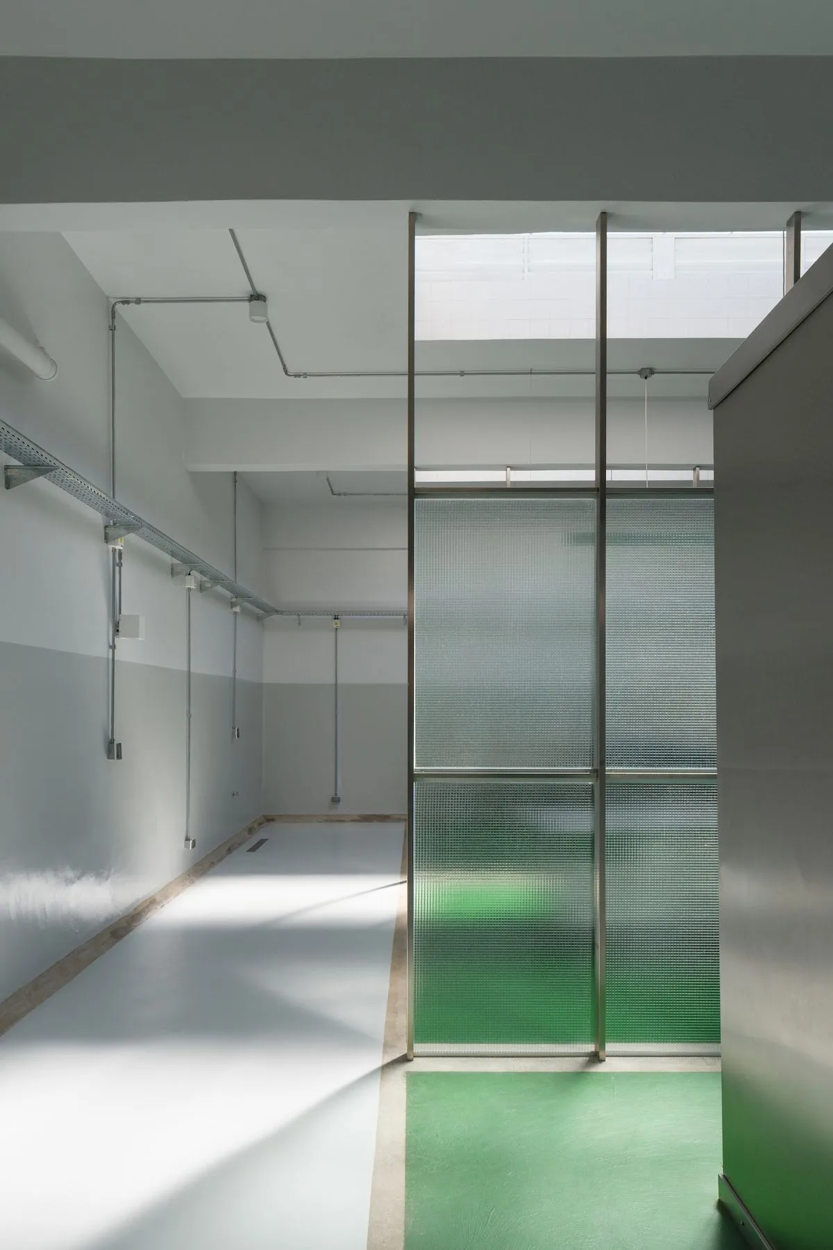 Vue intérieure d'une dark kitchen avec cloisons de verre nervuré, sol résine vert et blanc contrastant, éclairage LED linéaire