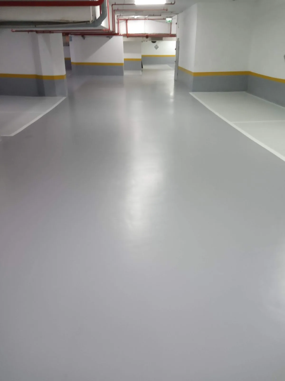 Vue longitudinale d'un couloir de parking en résine finition brillante avec plinthes jaune et grise, pose fraîchement terminée